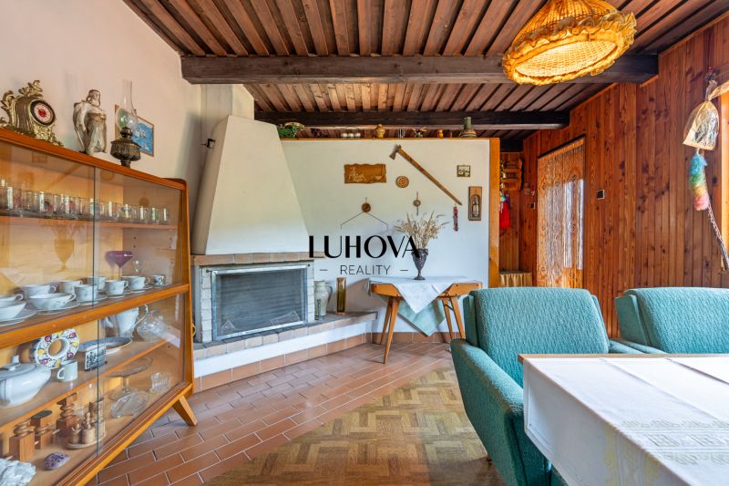Interior of a cabin with a fireplace, display cabinet, green armchairs, and a wooden-patterned floor.
