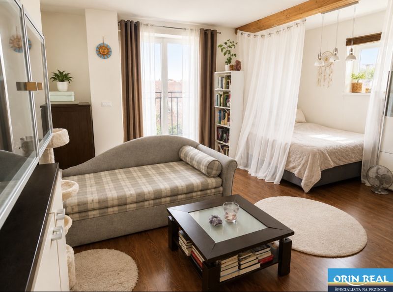 A bright living space in a studio apartment with wood-patterned flooring and a comfortable sofa.