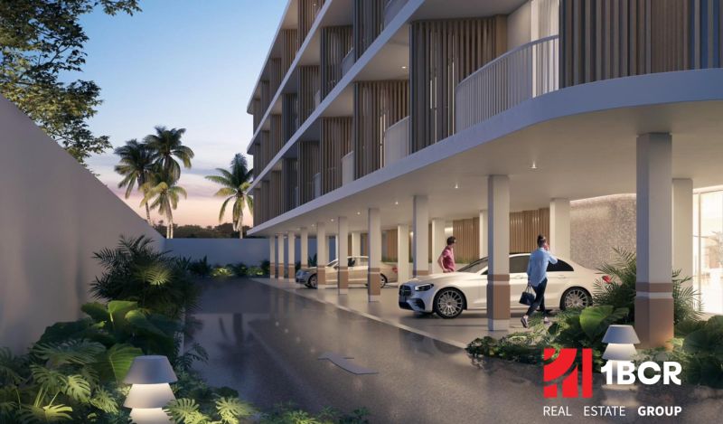 Apartment construction in Surat Thani: parking under a modern building surrounded by tropical greenery.