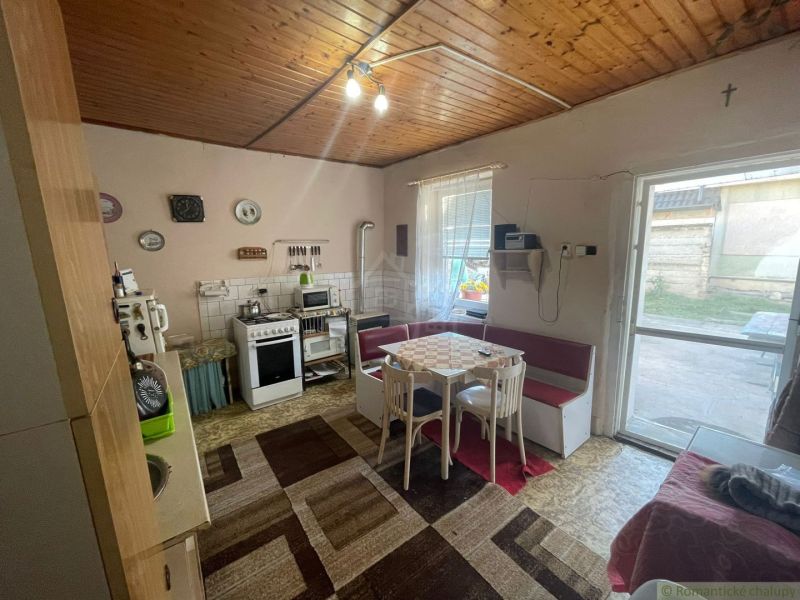 A kitchen in a family house with a dining table, carpets, and a wooden ceiling.