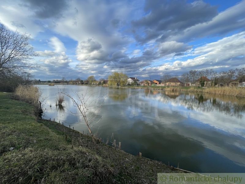 A calm water surface with family houses in Tvrdošovce and a dramatic sky.