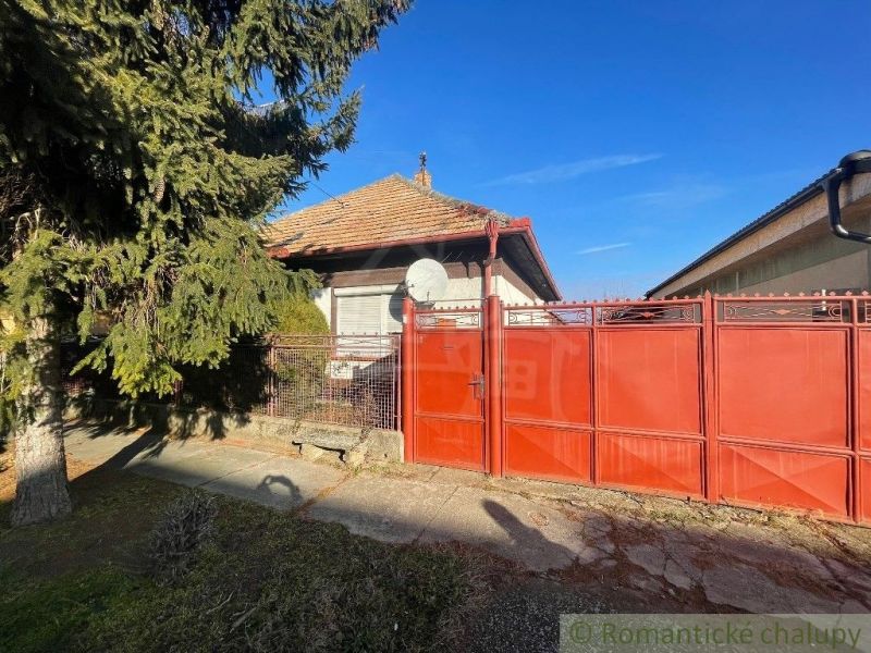 Red gate and fence with a family house in Tvrdošovce, surrounded by greenery.
