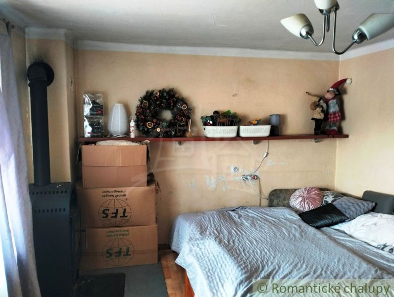 A room with a bed, a shelf, cardboard boxes, and a stove in a family house.