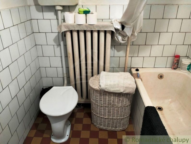 A bathroom in a family house with a bathtub, toilet, radiator, and storage basket.