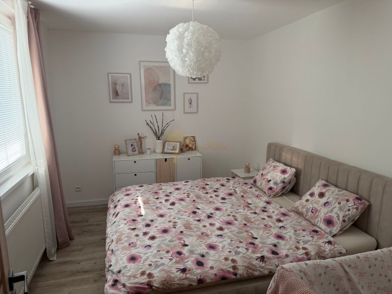 A bedroom with a bed, floral bedspread, and wood-patterned flooring in a 3-room apartment.