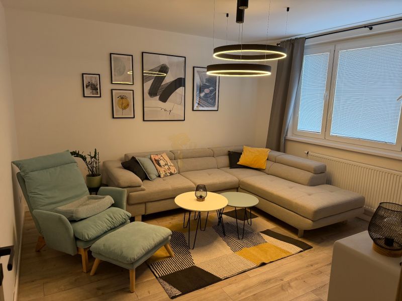 Living room with a gray sofa, armchair, and decorative paintings in a three-room apartment.