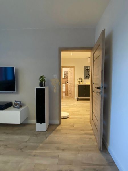 Living room in a three-room apartment with a wooden decor floor and a TV on the wall.