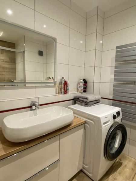 Bathroom in a 3-room apartment with a white sink and a washing machine on a wooden decor.