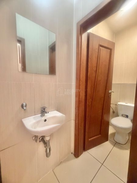 A small bathroom with a sink, mirror, and toilet in commercial premises.