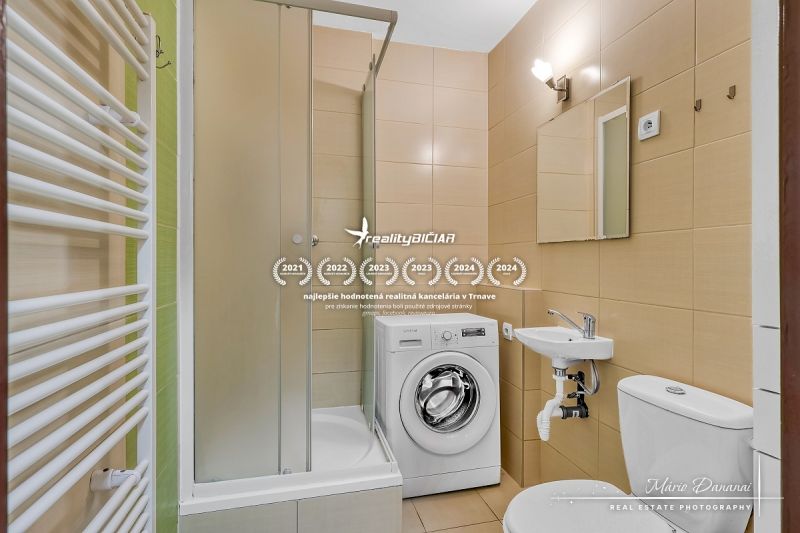 Bathroom in a studio apartment with a shower and a washing machine, beige tiles.
