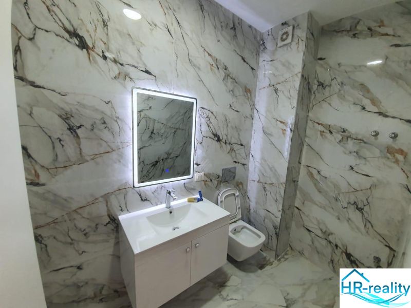 Bathroom in a holiday apartment with marble decor and a mirror with LED backlighting.