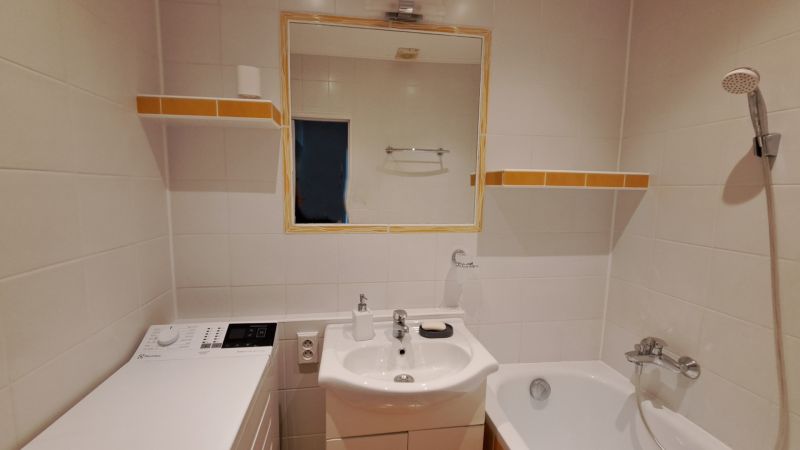 Bathroom with a sink, mirror, washing machine, and bathtub in a two-room apartment.