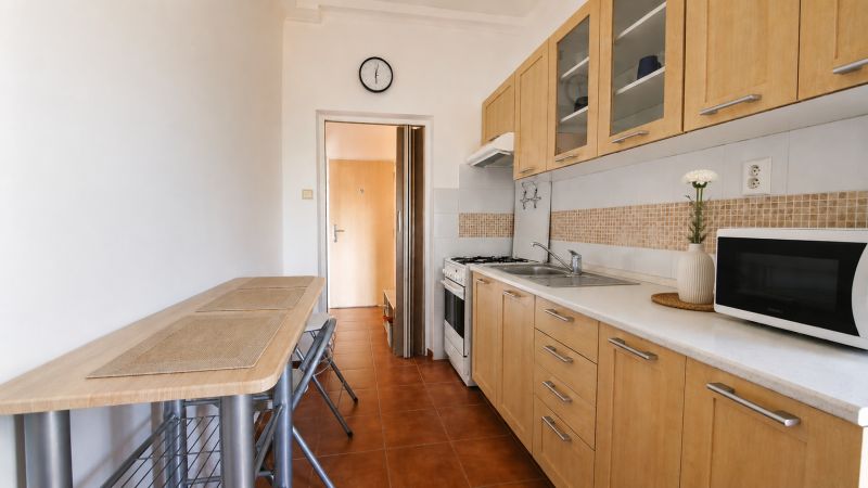 A kitchen in a 2-room apartment with wooden cabinets and a microwave.