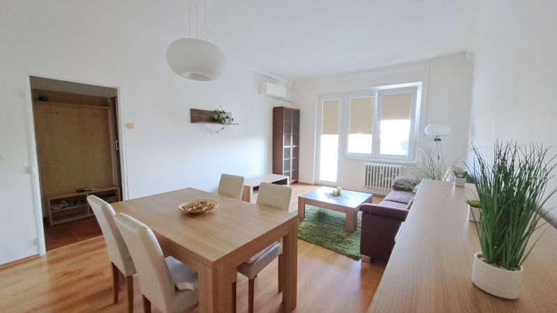 Living room in a two-room apartment with a wooden decor floor and a dining table.