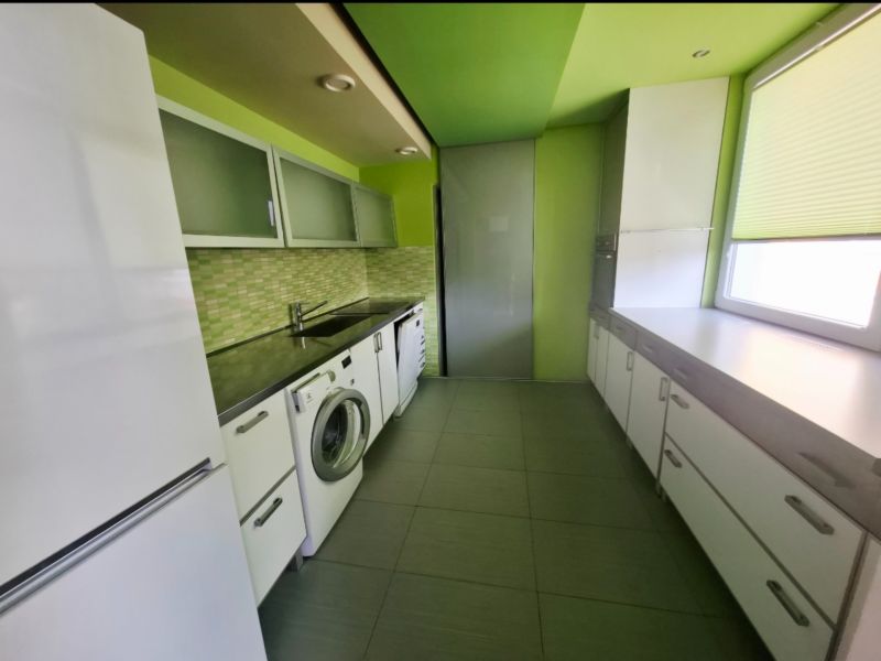 A kitchen in a 3-room apartment with a washing machine, white furniture, and green walls.