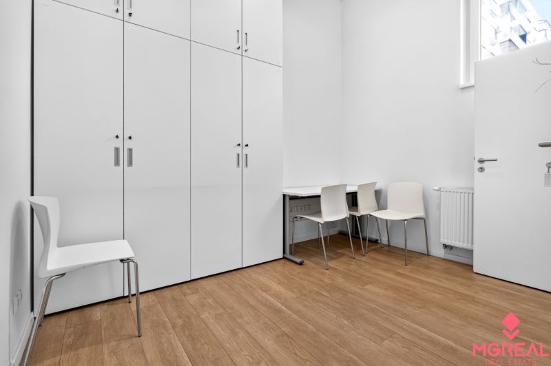 White cabinets, chairs, and a table on a wooden decor floor in commercial premises.
