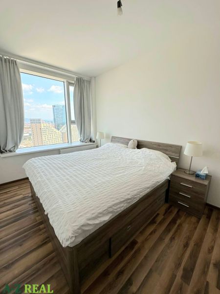 A room with a large window, a bed, and a floor with a wooden decor in a 3-room apartment.