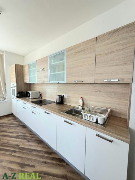 A kitchen unit with white cabinets and a wooden decor floor in a 3-room apartment.