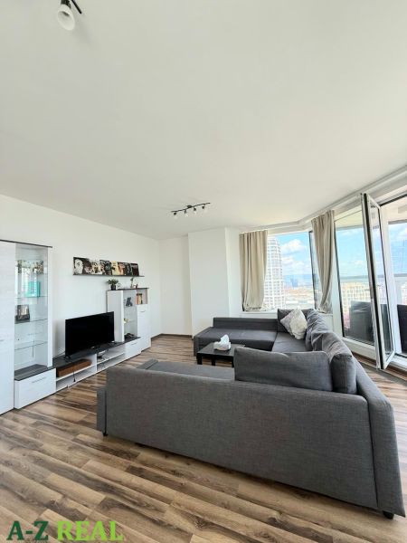 Living room with wood-patterned flooring, a sofa, and a television in a three-room apartment.
