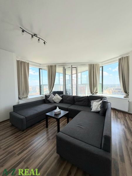 Spacious living room area with a dark sofa and wooden decor flooring in a 3-room apartment.