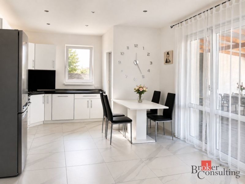 A kitchen in a family house with white furniture and decorative clocks on the wall.