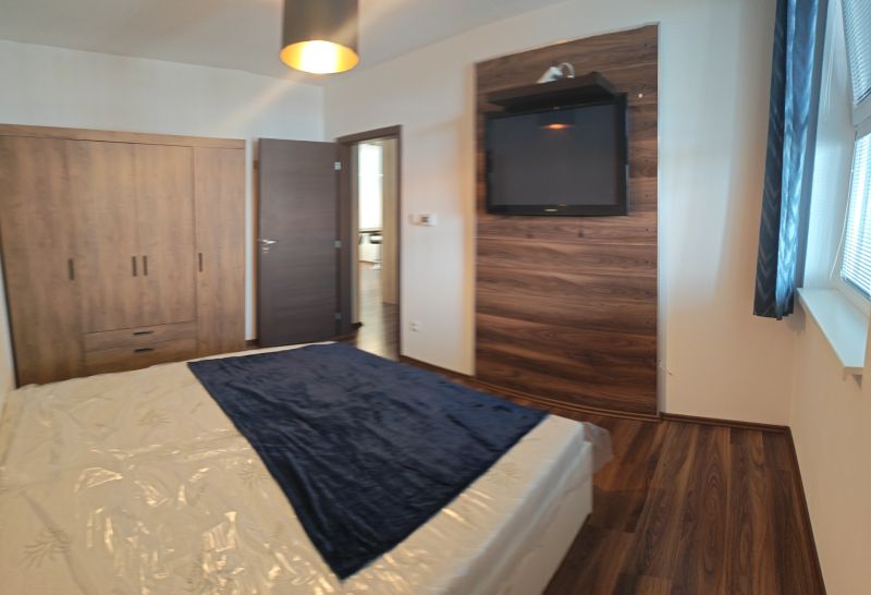 Bedroom of a two-room apartment with a wooden decor floor, a television, and a wardrobe.