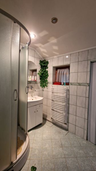 A bathroom with tiles, a shower, a sink, and a radiator, furnished in a family house.
