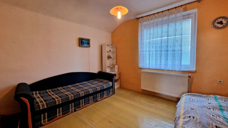 Living room in a family house with a sofa, a shelf, and a curtain behind the window.