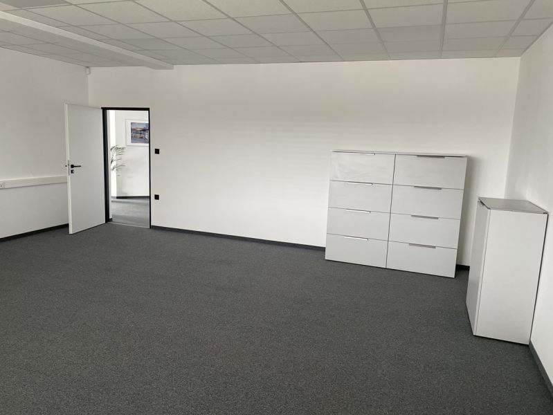 A white office with a dark gray carpet, light furniture, and open doors.