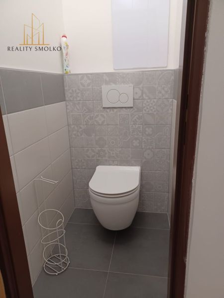 A toilet in a 2-room apartment with decorative wall tiles and a gray floor.