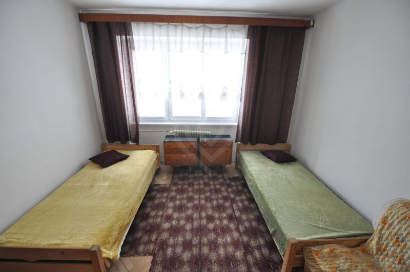 A bedroom with two single beds, a carpet, and a window in a 2-room apartment.