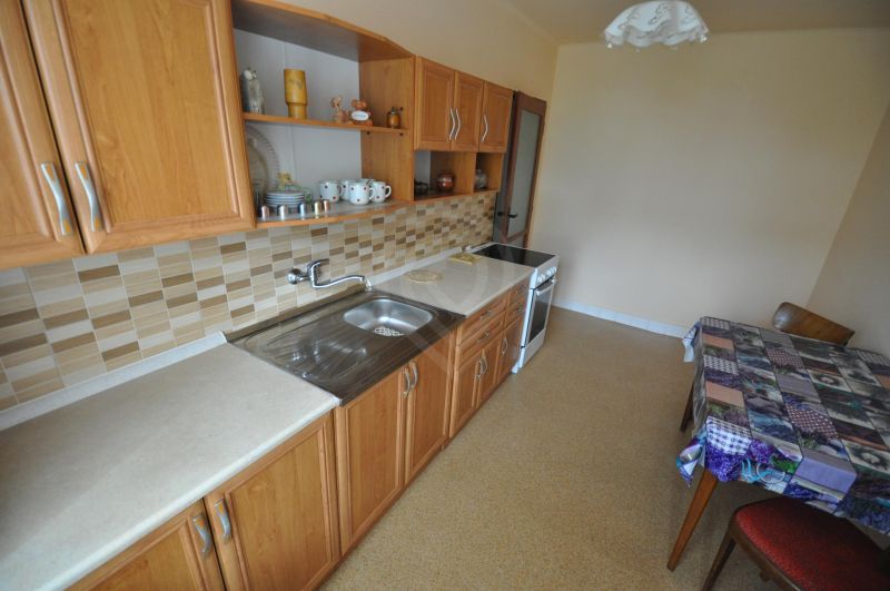 A kitchen in a 2-room apartment with wooden cabinets and tiled backsplash.