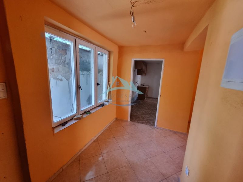 An orange-painted hallway with windows and tiles, leading to another room in a family house.