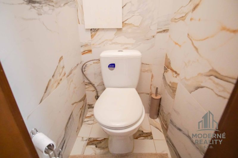 A toilet in a bathroom with marble tiles in a 2-room apartment.