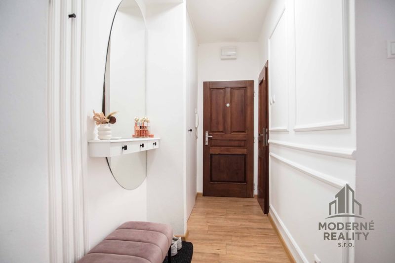 The hallway of a 2-room apartment with a wooden decor floor and a mirror on the wall.
