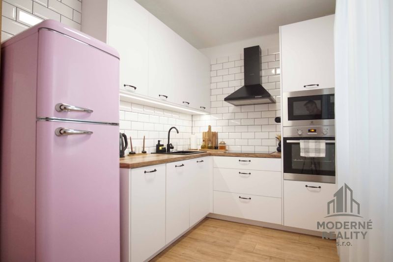 A kitchen in a 2-room apartment with a pink refrigerator and a wooden decor floor.