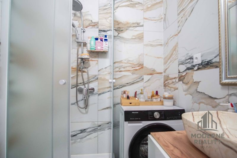 A bathroom in a 2-room apartment with marble tiles, a shower corner, and a washing machine.