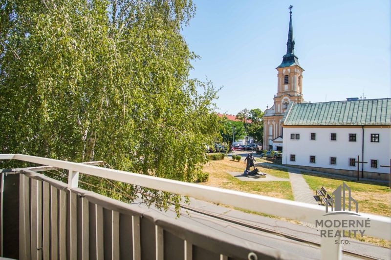 View from the balcony in Nové Zámky, near a 2-room apartment, with a church and greenery.
