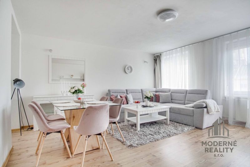 Living room in a two-room apartment with a wooden decor floor, gray sofa, and dining table.
