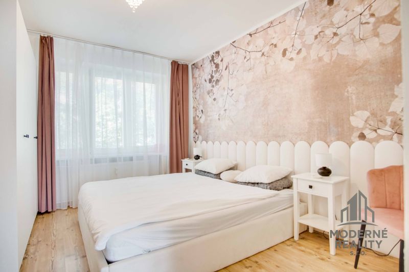 Bedroom in a two-room apartment with a wooden decor floor and subtle wallpaper.