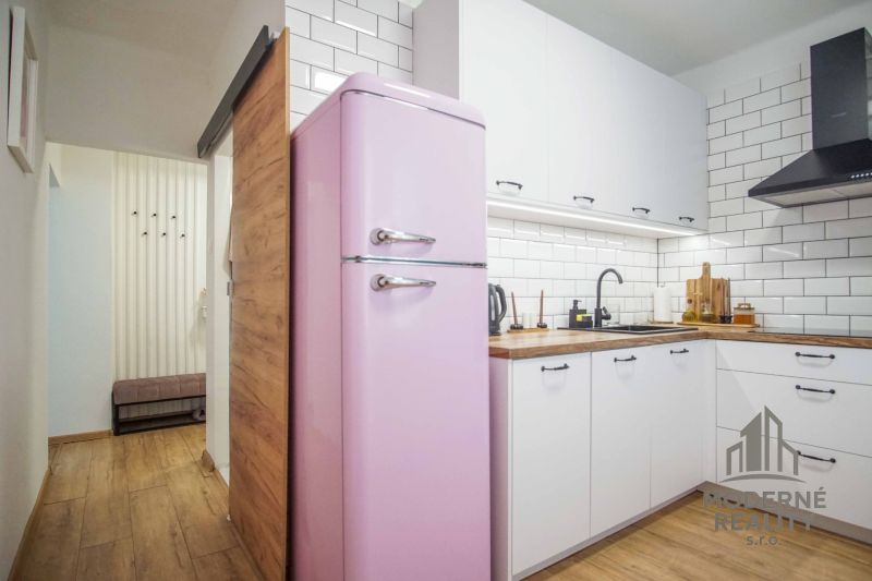 A kitchen in a 2-room apartment with a retro pink refrigerator and a wooden decor floor.