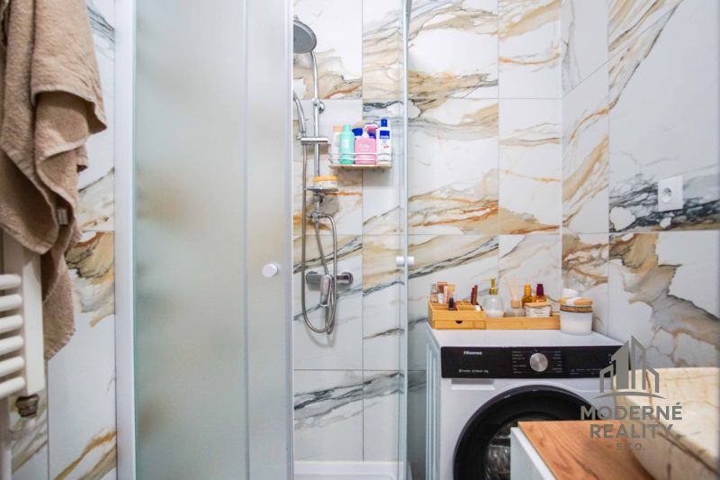 Bathroom in a 2-room apartment with a washing machine and shower, surrounded by marble tiles.
