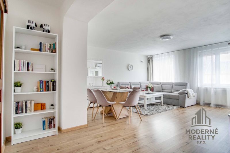 Living room in a two-room apartment with a wooden decor floor, light seating, and a bookshelf.