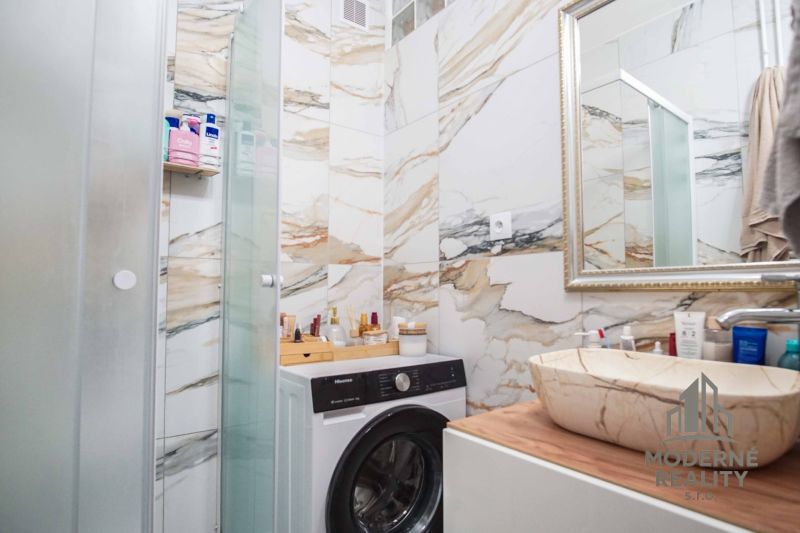Bathroom of a 2-room apartment with a washing machine, sink, and marble tiles.