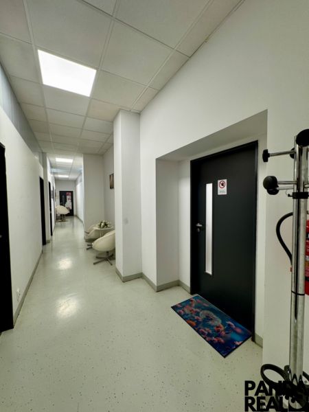 A corridor of commercial spaces with light walls, decorative mats, and wall lights.