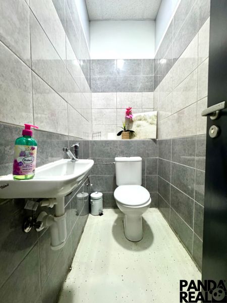 Bathroom in commercial premises with a toilet, sink, and decorative flower on a shelf.