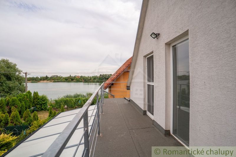 A cottage in Senec with a balcony and a view of the lake, surrounded by greenery.