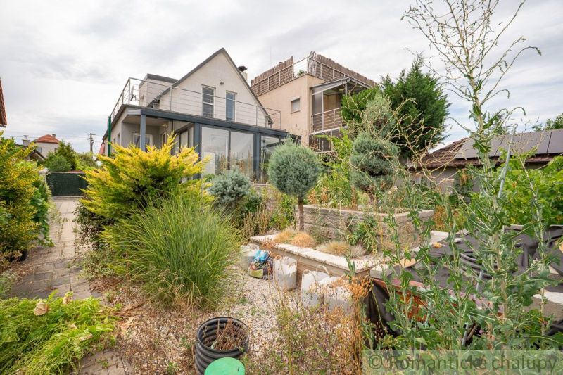 A cottage in Senec with a garden, green plants, and a terrace on the upper floor.