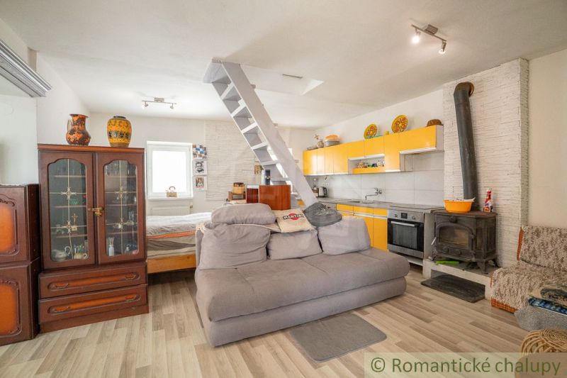 The interior of the cabin with a kitchenette, stove, sofa, and staircase with wooden decor.