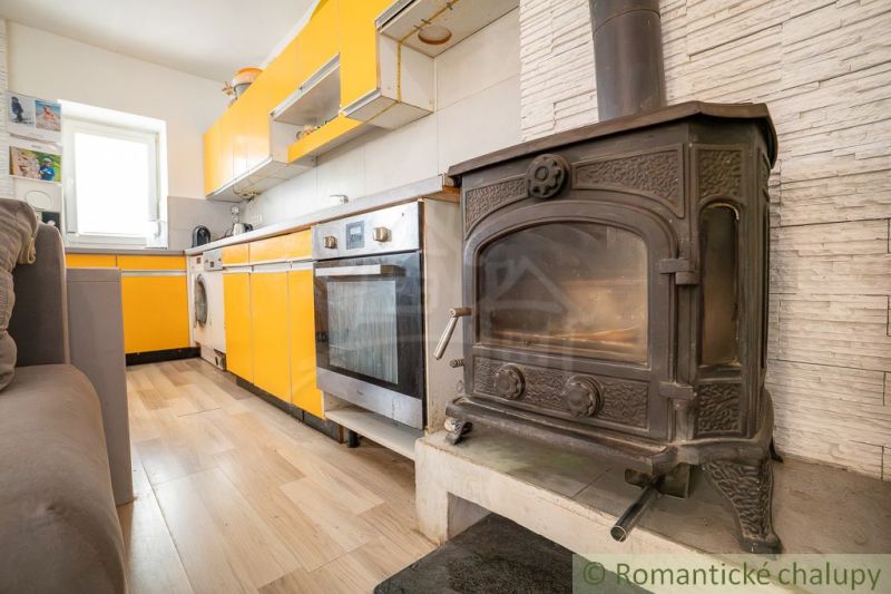 A kitchen in a cottage with an orange kitchen unit and a tiled stove, and a floor with a wooden decor.